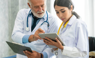 Senior male doctor using tablet computer while discussing with another doctor at the hospital. Medical healthcare staff and doctor service.