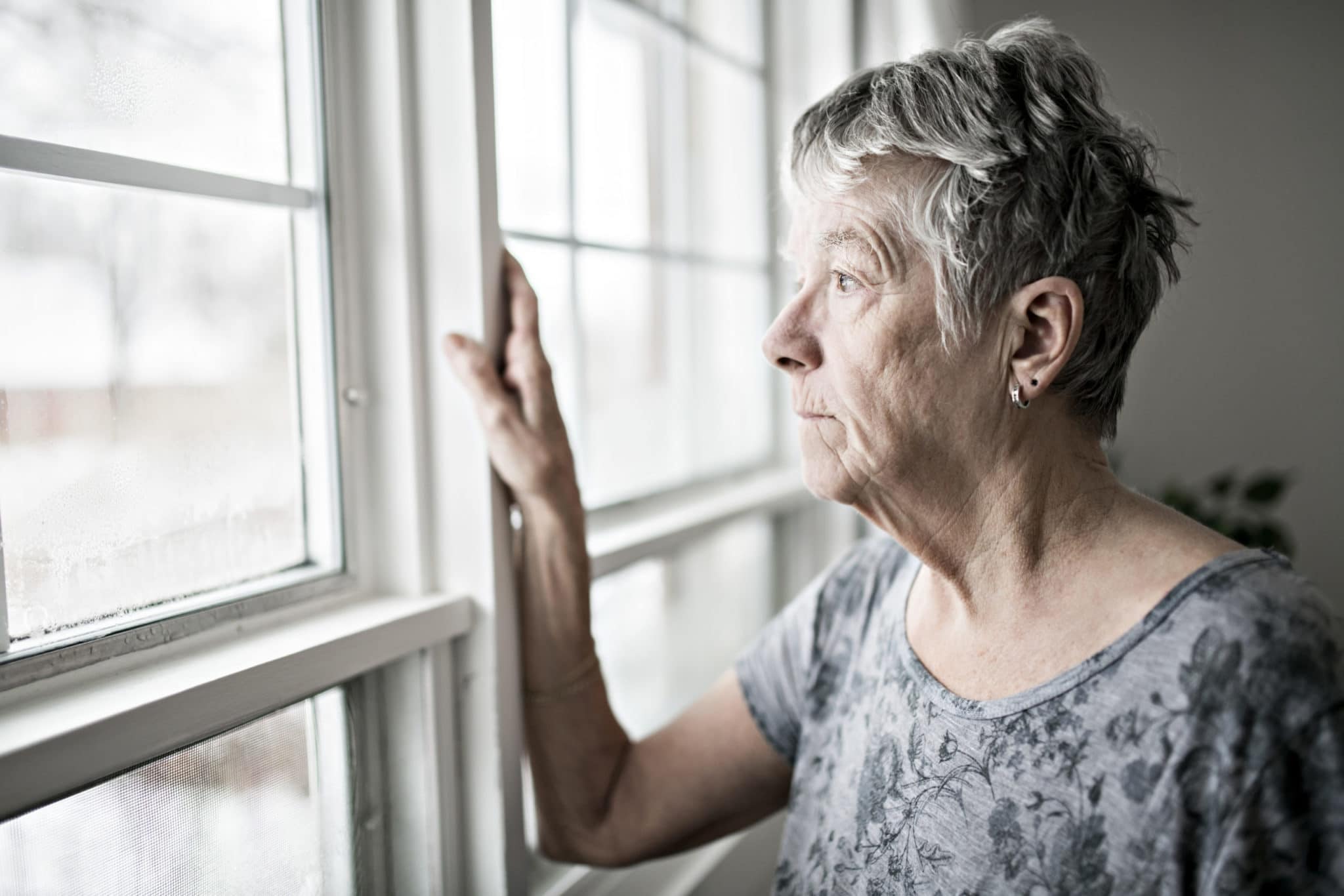 A lonely senior woman looks out the window.