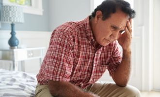 Senior Hispanic Man Sitting On Bed Suffering With Depression