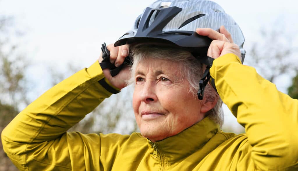 An elderly woman putting on a helmet