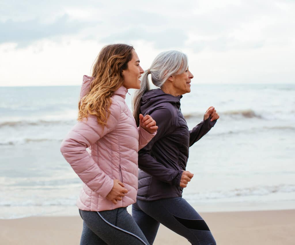 Mother and daughter jogging along the beach in light sport jackets, promoting healthy lifestyle choices and cognitive health